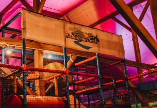 Indoor-Spielplatz mit farbenfroher Beleuchtung und Camping De Rammelbeek-Banner im Ferienpark Overijssel.