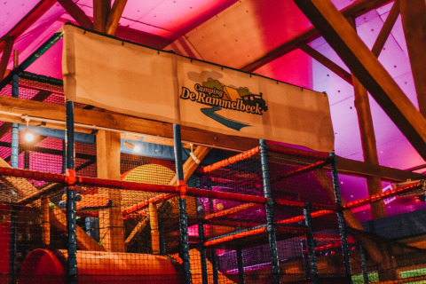 Indendørs legeplads med farverig belysning og Camping De Rammelbeek-banner på en feriepark i Overijssel.