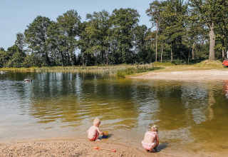 Zwei Kinder spielen am Seeufer im Ferienpark Camping De Rammelbeek, Overijssel, Niederlande, im Grünen.