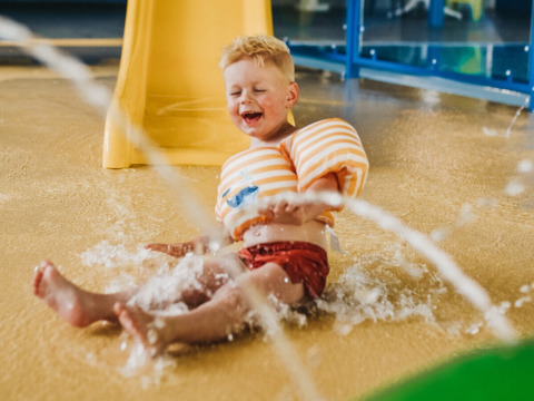 Un bambino con braccioli si diverte nell’area giochi d’acqua di Camping De Rammelbeek, Overijssel, Paesi Bassi.