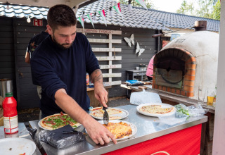 Uomo che prepara la pizza fresca in un forno a legna al Camping Emmen, un parco vacanze a Drenthe, Paesi Bassi.