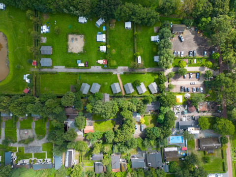 Vista aérea del parque vacacional Camping Emmen en Drenthe, Países Bajos, con tiendas y cabañas verdes.