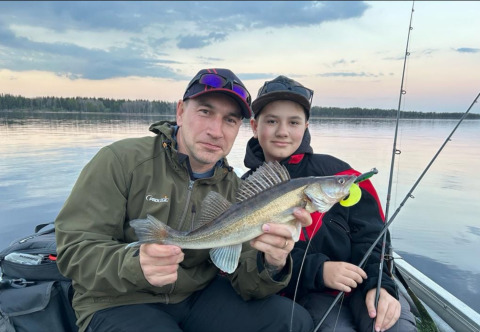 Dos personas sostienen un pez recién capturado mientras pescan al atardecer en el lago de Camping Falkudden.