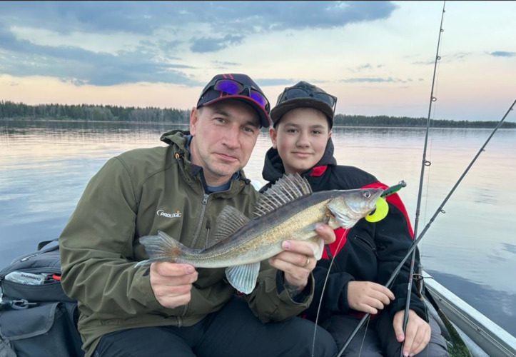 Deux personnes tiennent un poisson fraîchement pêché sur un lac au coucher du soleil au Camping Falkudden.