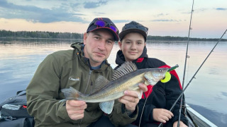 Dos personas sostienen un pez recién capturado mientras pescan al atardecer en el lago de Camping Falkudden.