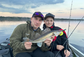 Dos personas sostienen un pez recién capturado mientras pescan al atardecer en el lago de Camping Falkudden.