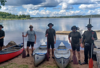 Five people stand by three canoes on a lakeshore at Camping Falkudden holiday park in Dalarna, Sweden.