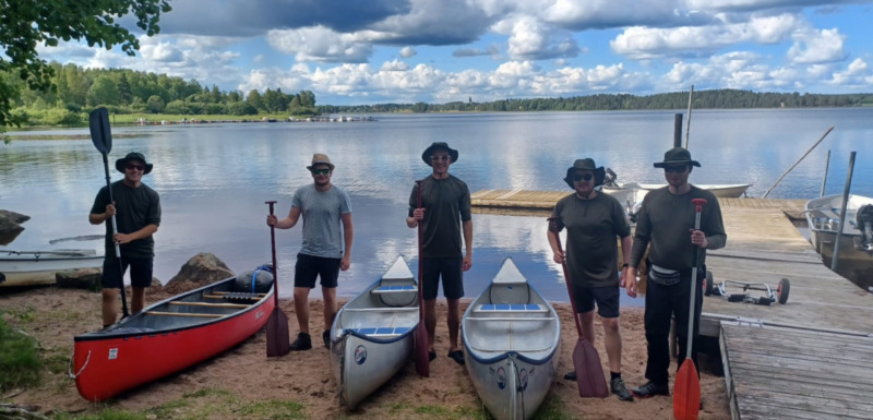 Cinq personnes posent avec des canoës au bord d’un lac à Camping Falkudden, Dalarna, Suède.