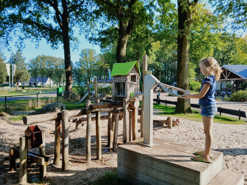Ein Kind spielt bei sonnigem Wetter an einer Wasserpumpe im Familiepark de Vechtvallei, Overijssel.