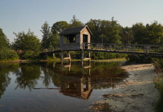 Holzbrücke mit kleinem Häuschen über einem ruhigen Teich in Familiepark de Vechtvallei, Overijssel, Niederlande.