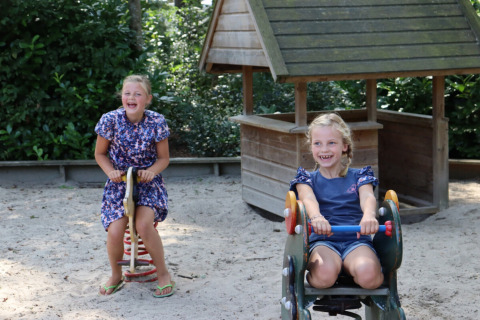 Dos niñas sonrientes juegan en balancines de un parque de arena en Familiepark de Vechtvallei, Overijssel.