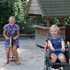 Dos niñas sonrientes juegan en balancines de un parque de arena en Familiepark de Vechtvallei, Overijssel.