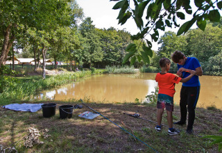 To personer fisker ved en sø i Familiepark de Vechtvallei, Overijssel, omgivet af træer og natur.