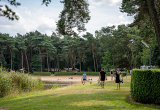 Familien spazieren zum Sandstrand am See im Ferienpark Goolderheide, Limburg, Belgien, umgeben von Wald.