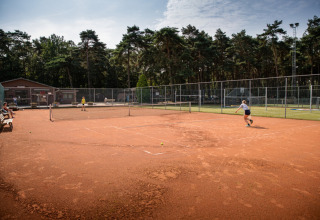Two people play tennis on a clay court at Familiepark Goolderheide holiday park in Limburg, Belgium.