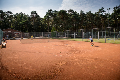 Two people play tennis on a clay court at Familiepark Goolderheide holiday park in Limburg, Belgium.