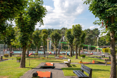 Familiepark Goolderheide con campo de minigolf, piscina, bancos y árboles en un entorno verde en Bélgica.