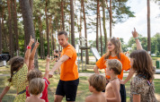 Børn og to voksne leger sammen i en skovklædt legeplads på Familiepark Goolderheide i Belgisk Limburg.