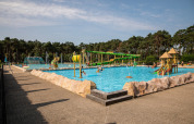 Børnevenligt udendørs swimmingpoolområde i Familiepark Goolderheide, omgivet af træer og rutsjebaner.
