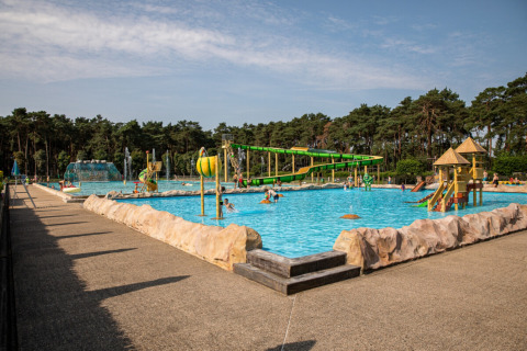 Børnevenligt udendørs swimmingpoolområde i Familiepark Goolderheide, omgivet af træer og rutsjebaner.