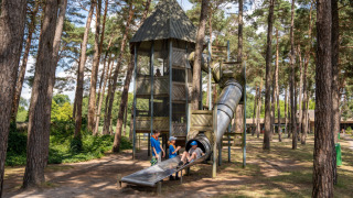 Kinder spielen auf einem Abenteuerspielplatz mit Rutsche und Turm im Waldpark Familiepark Goolderheide.