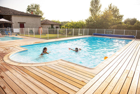 Piscina all'aperto con due persone, terrazza in legno e recinzione a Camping Fargogne, Occitanie, Francia.