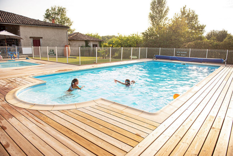 Swimmingpool mit zwei Personen, Holzdeck und Zaun im Ferienpark Camping Fargogne in Occitanie, Frankreich.