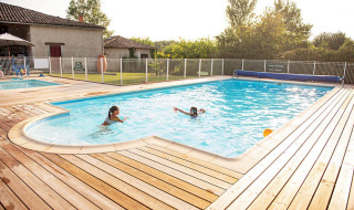 Piscina al aire libre con dos personas, terraza de madera y valla en Camping Fargogne, Occitanie, Francia.