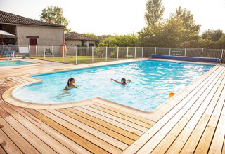 Outdoor swimming pool with two people, wooden decking and fence at Camping Fargogne holiday park, Occitanie, France.
