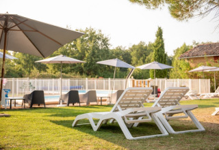 Lettini e ombrelloni presso la piscina di Camping Fargogne, villaggio vacanze in Occitania, Francia.