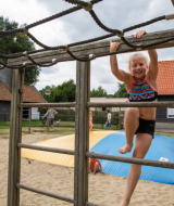 Kind spielt auf einem Klettergerüst im Sand auf Camping Gorishoek, einem Ferienpark in Zeeland, Niederlande.