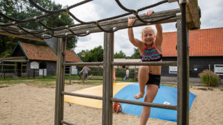 Kind spielt auf einem Klettergerüst im Sand auf Camping Gorishoek, einem Ferienpark in Zeeland, Niederlande.