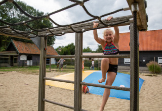 Kind spielt auf einem Klettergerüst im Sand auf Camping Gorishoek, einem Ferienpark in Zeeland, Niederlande.