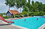 Udendørs swimmingpool med børn og voksne på Camping Gorishoek i Zeeland, Holland, omgivet af grønne træer.