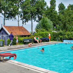 Außenpool mit Kindern und Erwachsenen im Camping Gorishoek, Zeeland, Niederlande, umgeben von Bäumen.