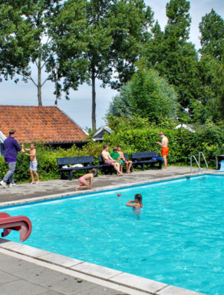 Außenpool mit Kindern und Erwachsenen im Camping Gorishoek, Zeeland, Niederlande, umgeben von Bäumen.