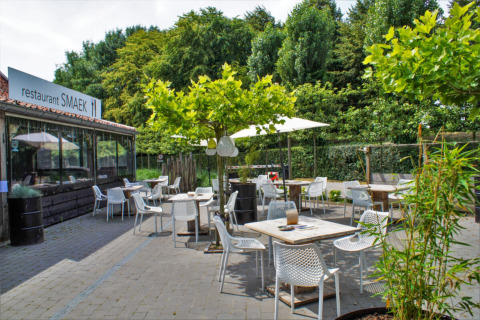 Terraza exterior del restaurante SMAEK en Camping Gorishoek, Zelanda, Países Bajos, rodeada de vegetación.