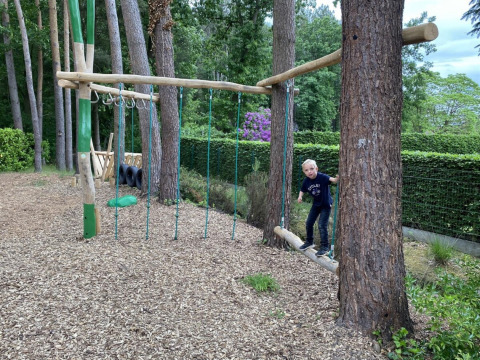 A child plays on a wooden adventure playground surrounded by trees at Camping het Swinnenbos, Belgium.