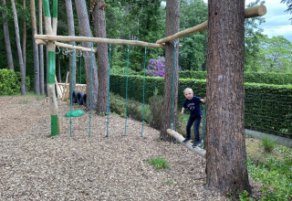 A child plays on a wooden adventure playground surrounded by trees at Camping het Swinnenbos, Belgium.