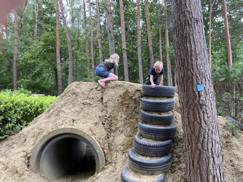 Two children play on a dirt hill with tire steps and a tunnel at Camping het Swinnenbos, Belgium.