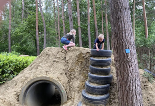 Two children play on a dirt hill with tire steps and a tunnel at Camping het Swinnenbos, Belgium.