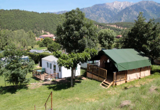 Campsite scene at Camping le Rotja, Occitanie, France, featuring tent and mobile home with mountain views.