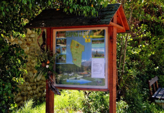Bacheca informativa al Camping le Rotja, villaggio turistico in Occitania, Francia, tra piante verdi.