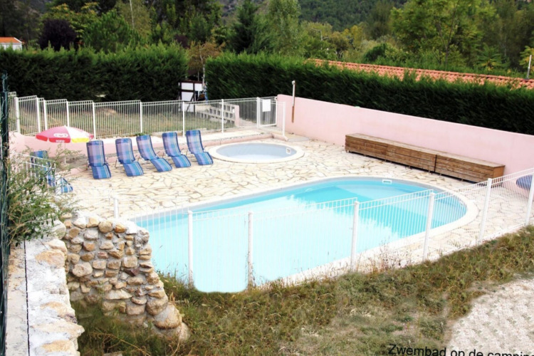 Outdoor swimming pool and children's pool with loungers and umbrella at Camping le Rotja in Occitanie, France.