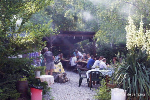 Reunión de barbacoa al aire libre en Camping le Rotja, Occitania, Francia, con invitados disfrutando de la comida.