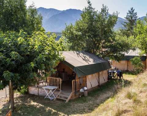Tende safari al Camping le Rotja in Occitania, Francia, circondate da alberi e montagne sullo sfondo.