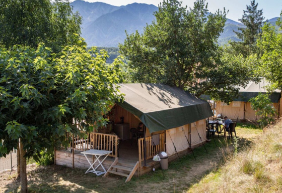 Safarizelte im Camping le Rotja, Occitanie, Frankreich, mit Bäumen und Bergen im Hintergrund.
