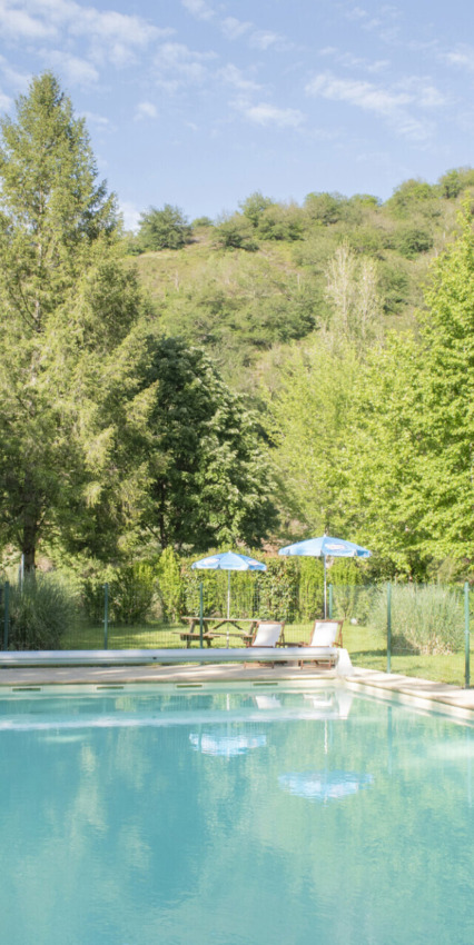Piscina all'aperto con lettini e ombrelloni in un parco vacanze tra le colline verdi, ideale per glamping.