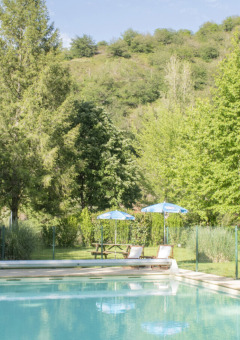 Piscina al aire libre con tumbonas y sombrillas en un parque de vacaciones ideal para glamping en la naturaleza.