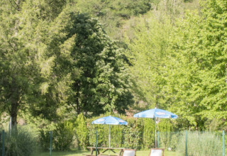 Poolbereich mit Sonnenliegen und Sonnenschirmen in einem Ferienpark mit Glamping und grüner Hügellandschaft.